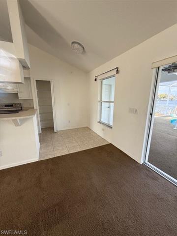 Unfurnished living room featuring light carpet and lofted ceiling