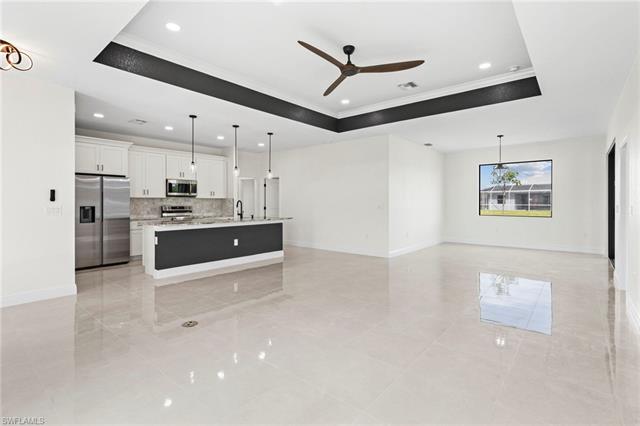 Kitchen featuring stainless steel appliances, hanging light fixtures, a center island with sink, a raised ceiling, and light tile floors