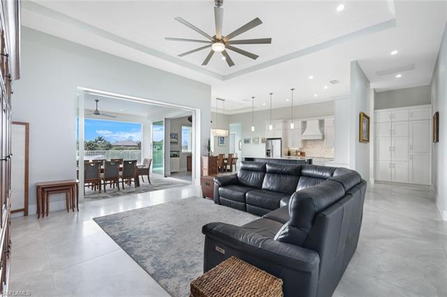 Living room with ceiling fan, a raised ceiling, and light tile patterned floors