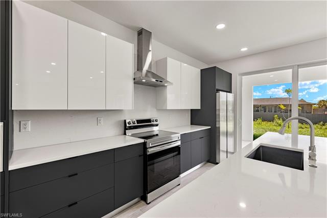 Kitchen featuring wall chimney range hood, sink, appliances with stainless steel finishes, and white cabinets