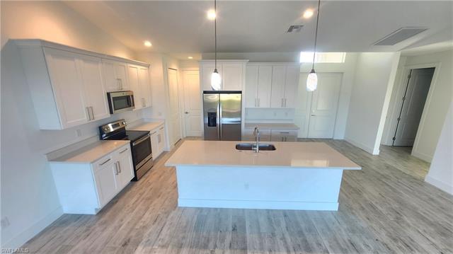 Kitchen featuring white cabinets, sink, stainless steel appliances, and an island with sink