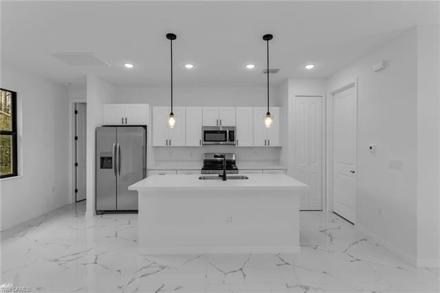 Kitchen featuring white cabinetry, sink, hanging light fixtures, stainless steel appliances, and a center island with sink