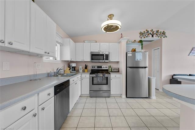 Kitchen featuring white cabinets, light tile patterned floors, appliances with stainless steel finishes, sink, and lofted ceiling
