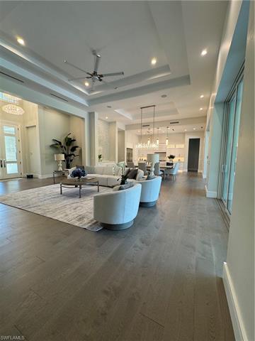 Unfurnished living room featuring dark wood finished floors, a tray ceiling, and ceiling fan with notable chandelier