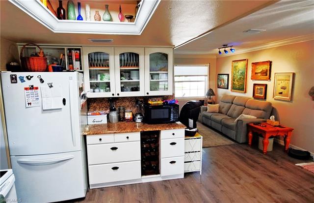 Kitchen with white cabinetry, crown molding, freestanding refrigerator, and black microwave