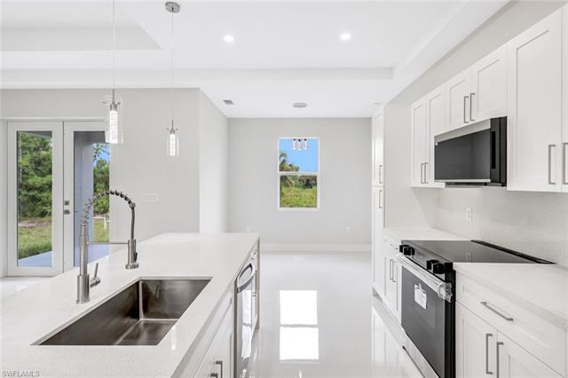 Kitchen featuring sink, white cabinetry, appliances with stainless steel finishes, decorative light fixtures, and light stone countertops