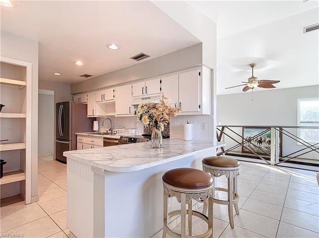 Kitchen with tasteful backsplash, a breakfast bar, kitchen peninsula, white cabinets, and light tile patterned floors