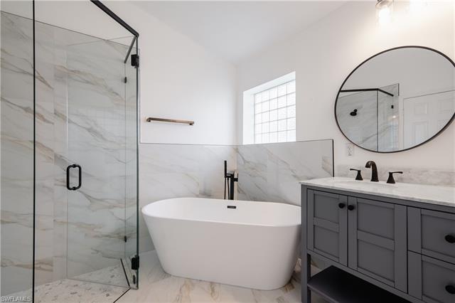 Bathroom featuring vanity, shower with separate bathtub, and tile walls