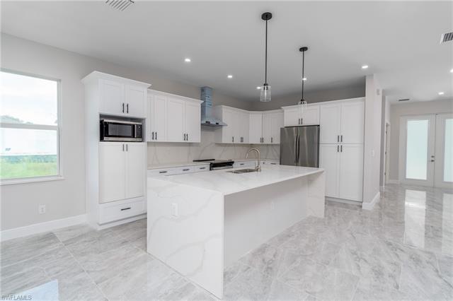 Kitchen featuring wall chimney exhaust hood, sink, a kitchen island with sink, white cabinetry, and appliances with stainless steel finishes