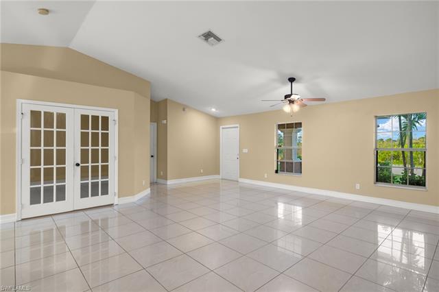 Empty room with light tile patterned floors, vaulted ceiling, french doors, and ceiling fan
