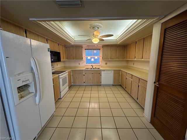 Kitchen featuring light tile patterned floors, ceiling fan, a raised ceiling, crown molding, and white appliances