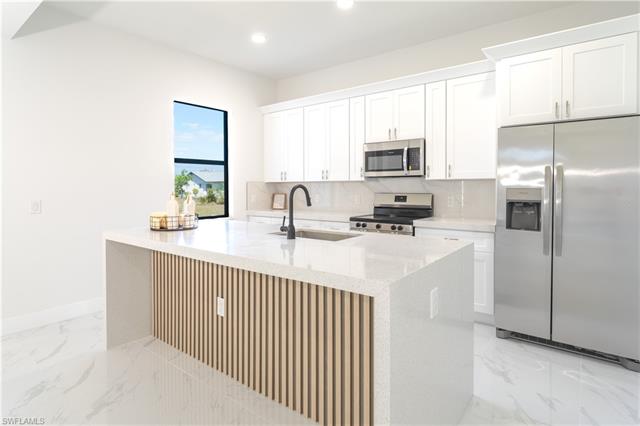 Kitchen with a kitchen island with sink, sink, white cabinets, and stainless steel appliances