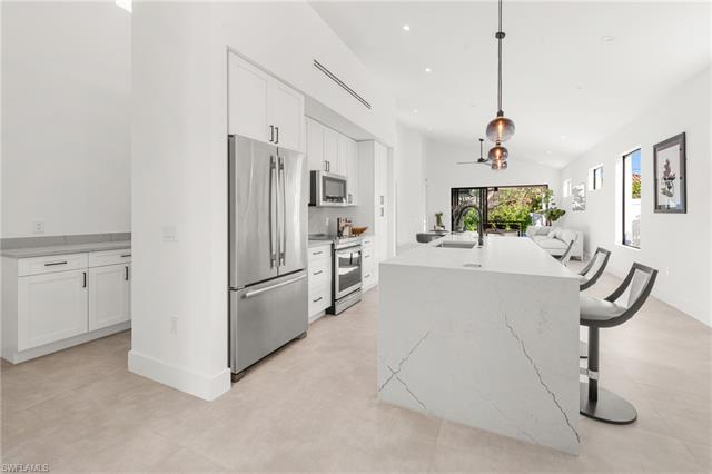 Kitchen featuring white cabinets, appliances with stainless steel finishes, open floor plan, a kitchen island with sink, and a sink