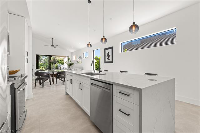 Kitchen featuring open floor plan, light stone countertops, stainless steel appliances, white cabinetry, and a sink