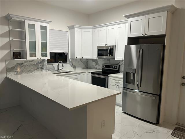 Kitchen with white cabinetry, sink, tasteful backsplash, kitchen peninsula, and appliances with stainless steel finishes