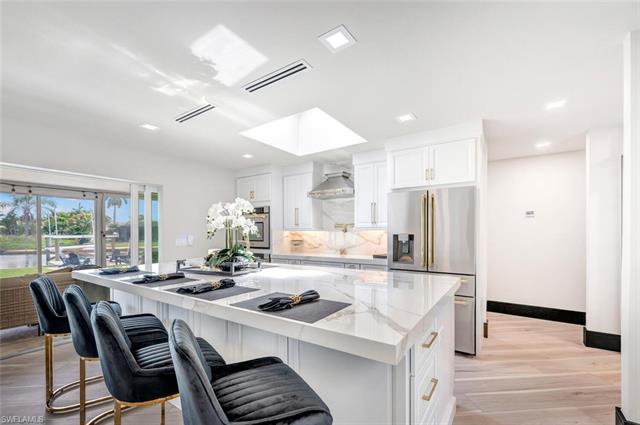 Kitchen with a skylight, white cabinets, light hardwood / wood-style flooring, light stone counters, and wall chimney exhaust hood
