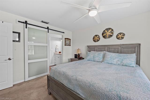 Bedroom featuring ceiling fan, connected bathroom, light carpet, and a barn door