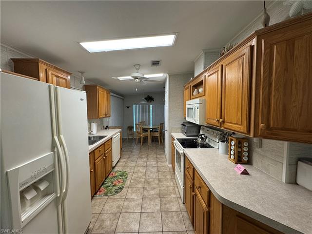 Kitchen featuring brown cabinets, backsplash, light tile patterned flooring, ceiling fan, and white appliances