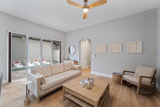 Living area with light wood-type flooring, baseboards, arched walkways, and a ceiling fan