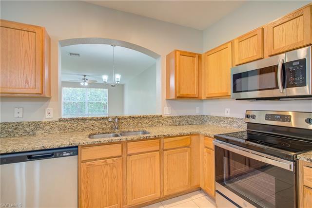 Kitchen with light tile patterned floors, arched walkways, appliances with stainless steel finishes, light stone counters, and a sink