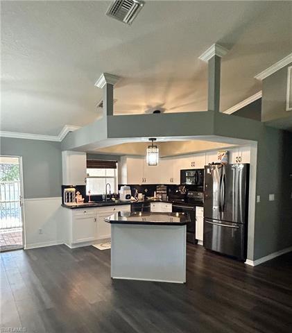 Kitchen with visible vents, dark countertops, freestanding refrigerator, black microwave, and range with electric stovetop