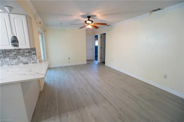 Unfurnished living room with light wood finished floors, visible vents, baseboards, a ceiling fan, and ornamental molding