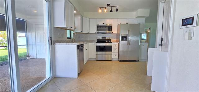 Kitchen featuring light tile patterned floors, a sink, white cabinets, appliances with stainless steel finishes, and decorative backsplash