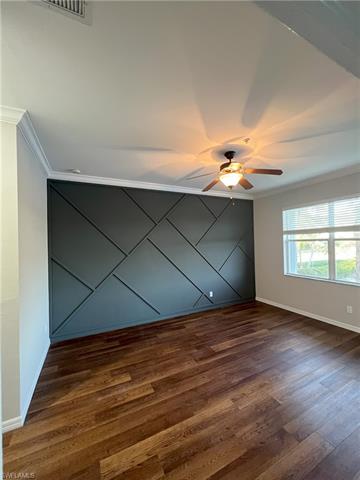 Empty room featuring visible vents, dark wood-type flooring, crown molding, baseboards, and ceiling fan