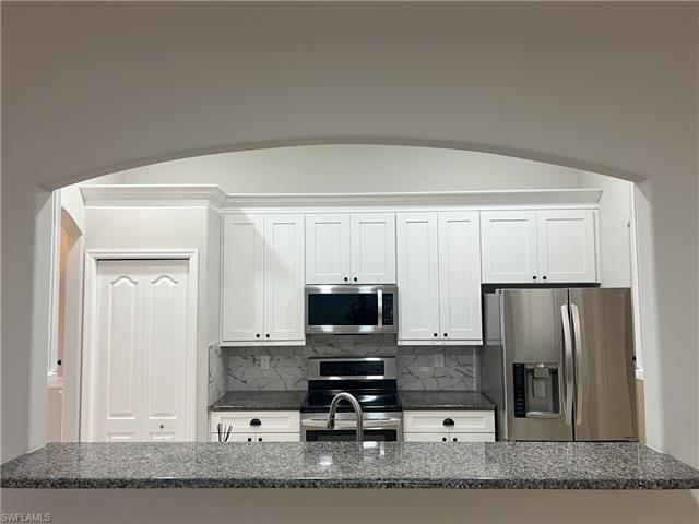 Kitchen with decorative backsplash, white cabinets, and appliances with stainless steel finishes