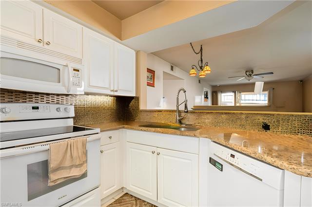 Kitchen featuring white appliances, light stone counters, a sink, decorative backsplash, and white cabinets