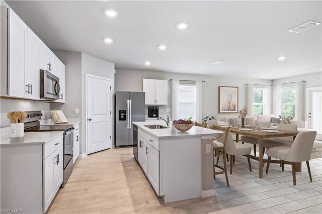 Kitchen featuring light wood-type flooring, stainless steel appliances, sink, a center island with sink, and white cabinetry