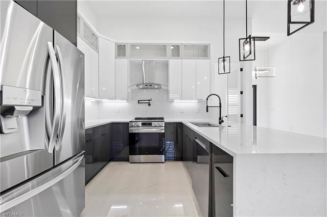 Kitchen with wall chimney exhaust hood, modern cabinets, appliances with stainless steel finishes, and a sink