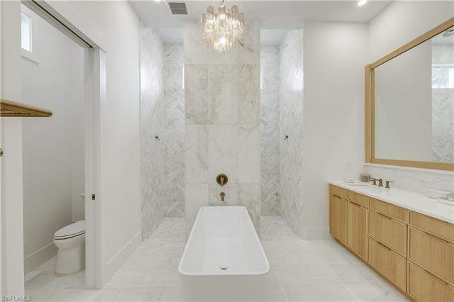 Bathroom with vanity, visible vents, toilet, walk in shower, and a notable chandelier