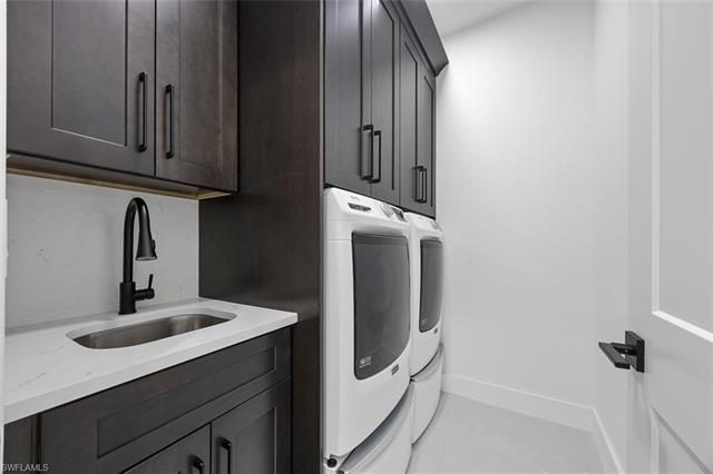 Laundry area with cabinet space, washer and dryer, baseboards, and a sink