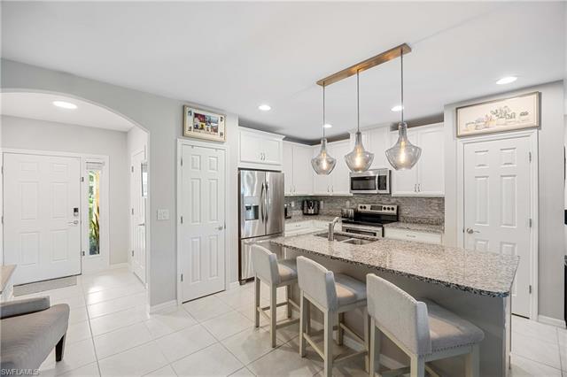 Kitchen featuring decorative light fixtures, light stone counters, tasteful backsplash, white cabinetry, and stainless steel appliances