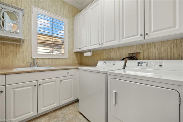 Clothes washing area with light tile patterned floors, washer and clothes dryer, a sink, and cabinet space