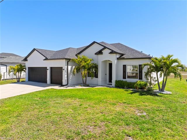 View of front of home with stucco siding, driveway, a front lawn, and a garage