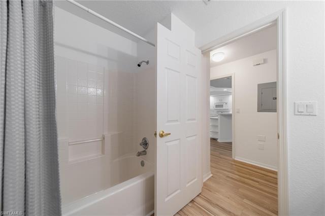 Bathroom featuring electric panel, shower / bathtub combination with curtain, baseboards, and wood finished floors