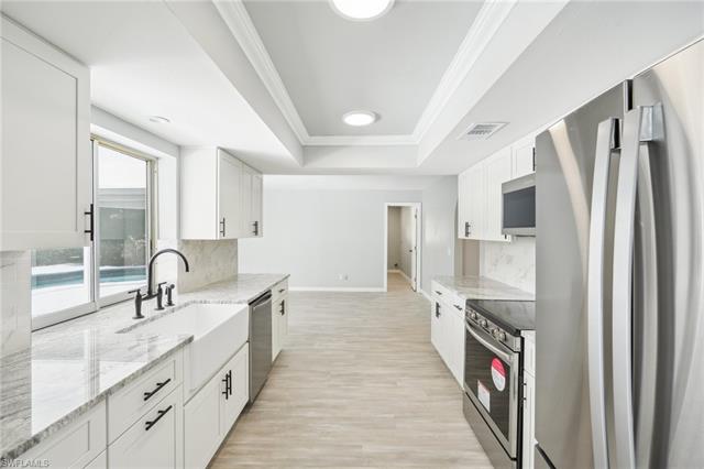 Kitchen with a tray ceiling, ornamental molding, a sink, appliances with stainless steel finishes, and white cabinetry