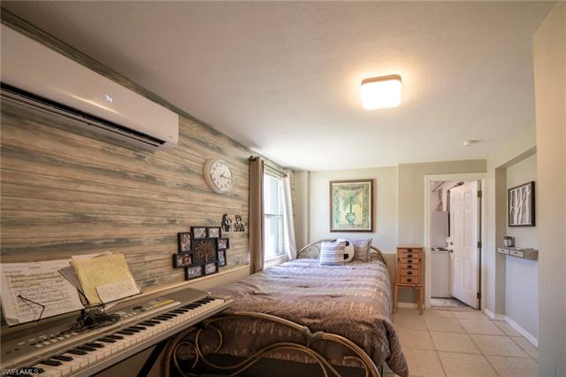 Bedroom with light tile patterned flooring, wood walls, an AC wall unit, and baseboards