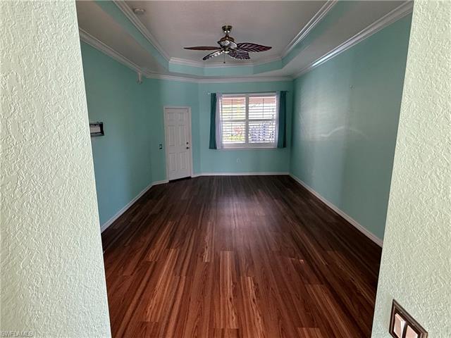 Unfurnished room featuring crown molding, baseboards, a tray ceiling, wood finished floors, and a ceiling fan