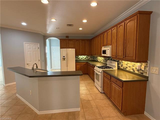 Kitchen featuring a sink, white appliances, dark countertops, and arched walkways