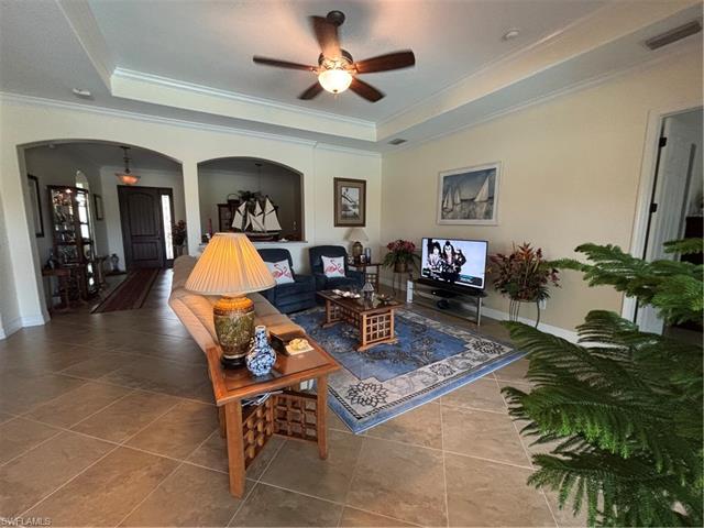 Tiled living area with visible vents, arched walkways, crown molding, a raised ceiling, and ceiling fan