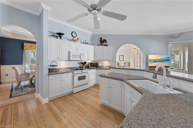 Kitchen featuring white appliances, arched walkways, a sink, crown molding, and light wood-type flooring
