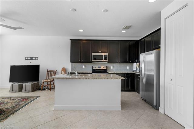 Kitchen with tasteful backsplash, light stone countertops, light tile patterned flooring, stainless steel appliances, and a kitchen island with sink
