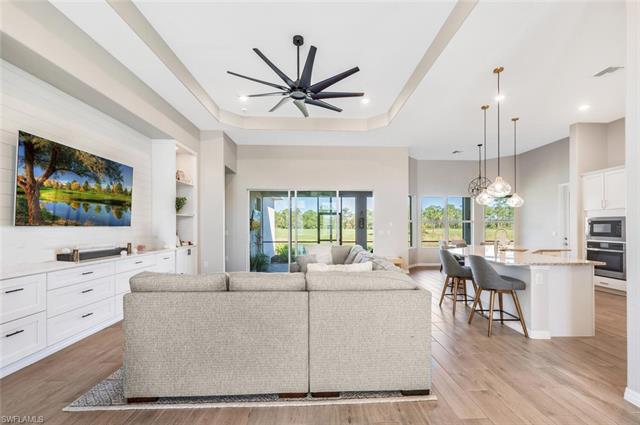 Living room with ceiling fan, a raised ceiling, sink, and light hardwood / wood-style flooring