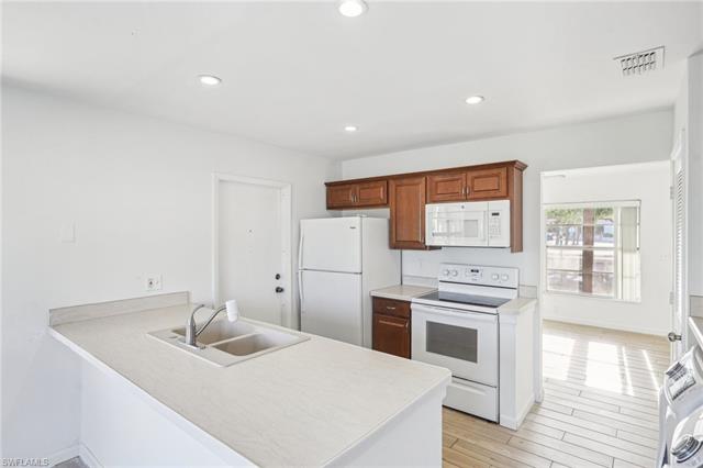 Kitchen with visible vents, light wood-style flooring, a sink, white appliances, and a peninsula