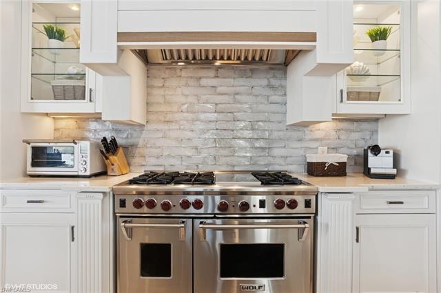 Kitchen featuring white cabinets, glass insert cabinets, wall chimney range hood, and range with two ovens