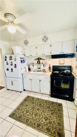 Kitchen with black electric range oven, light tile patterned floors, under cabinet range hood, and freestanding refrigerator