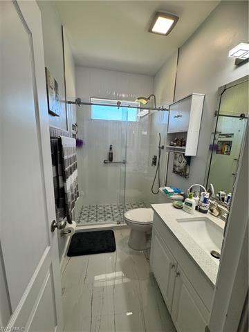 Bathroom with marble finish floor, toilet, a stall shower, and vanity